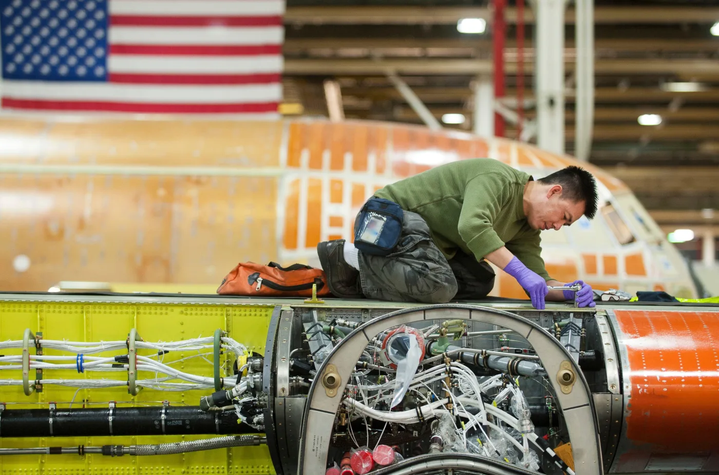 An aerospace technician working on an aircraft section beneath an American flag.
