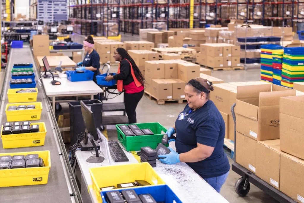 Warehouse workers scanning and packing goods along a fulfillment line.